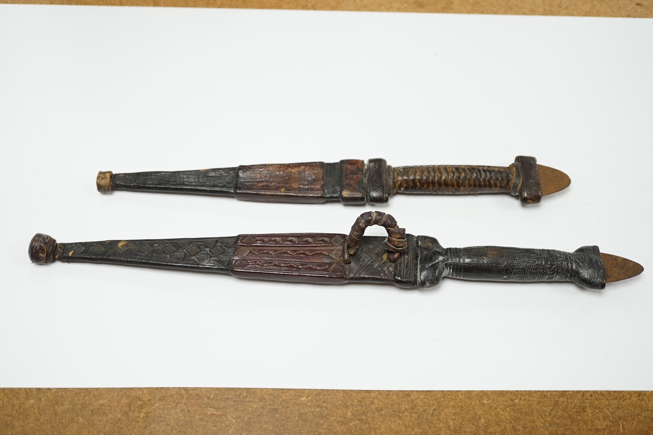 Two African Tuareg arm daggers, with leather grips and leather sheaths, longest blade 20cm. Condition - good